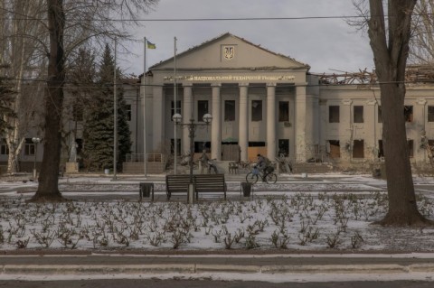 A man rides a bicycle past a university building destroyed by shelling in the city of Pokrovsk