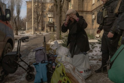 An elderly woman stands next to her belongings before boarding a minivan to be evacuated by volunteers and members of the Ukrainian police