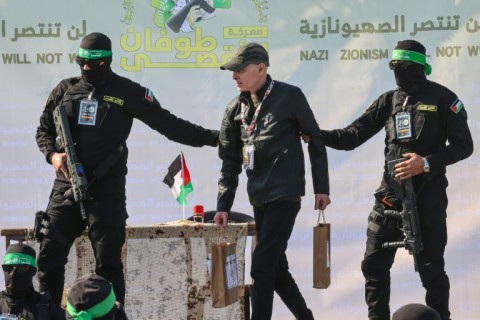 Palestinian militant group Hamas fighters escort American-Israeli hostage Keith Siegel on a stage before handing him over to a Red Cross team in Gaza City