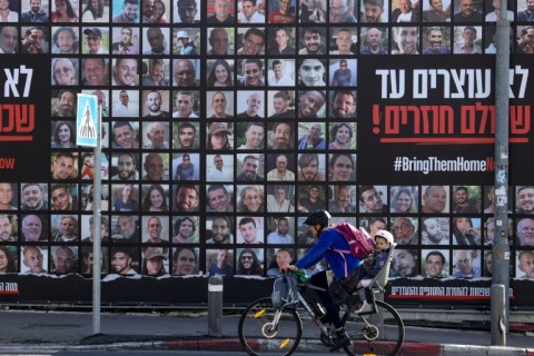 A man rides a bicycle past a billboard in Jerusalem featuring portraits of Israeli hostages held in the Gaza Strip