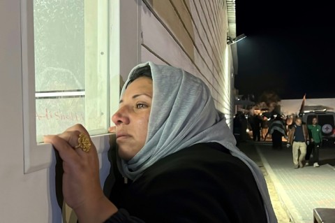 A Palestinian woman watches through a window as prisoners, released by Israel, arrive at the European Hospital in Khan Yunis, southern Gaza