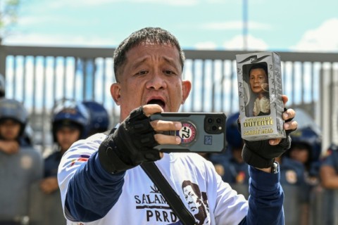 A supporter of former Philippine president Rodrigo Duterte films himself while holding a Duterte doll during a protest outside the Villamor Air Base