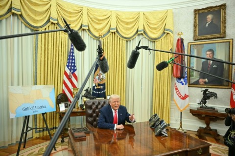 US President Donald Trump at the Resolute Desk, flanked by a map showing the "Gulf of America"