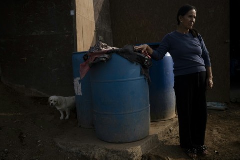 Catalina Naupa stands next to water drums outside her home on the southern outskirts of Lima