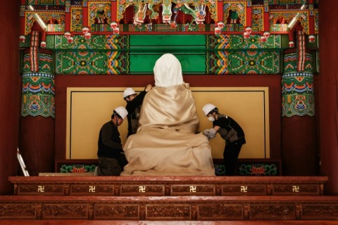 Members of the Gyeongbuk Seobu Cultural Heritage Care Center wrap a Buddha statue with cotton cloth and a fire-retardant blanket after evacuating all other items from the Gounsa Temple in Uiseong