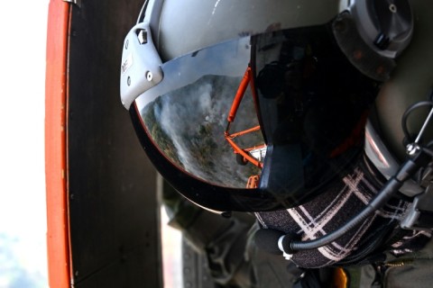 Smoke is reflected in a firefighter's visor, on board a helicopter used drop water on hard to reach areas