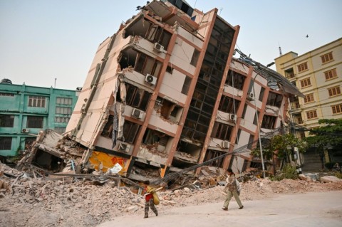 Children walk past a toppled building in Mandalay, five days after the deadly quake