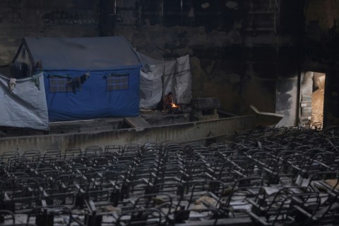 A displaced Palestinian woman cooks a meal on the stage of the auditorium in the heavily damaged Islamic University campus in Gaza City, where Palestinian families have taken refuge