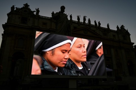 A screen shows an image of nuns during a rosary prayer on St Peter's Square