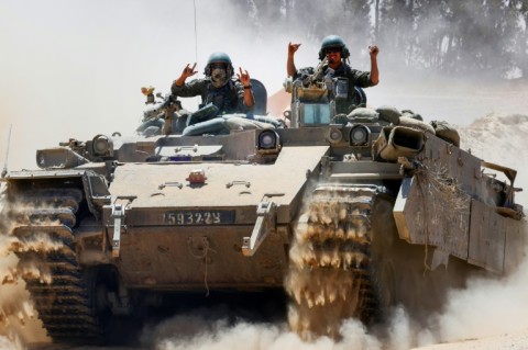 Israeli soldiers gesture atop a military vehicle at Israel's southern border with the Gaza Strip
