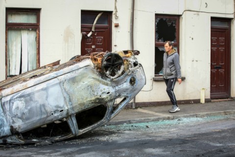 A pedestrian walks past a burnt car and a damaged house, after a second night of an anti-immigration demonstration in Ballymena, Northern Ireland