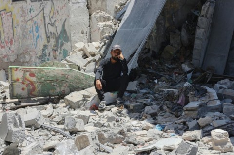 A Palestinian man sits amid the rubble of buildings destroyed in Israeli strikes on Gaza City