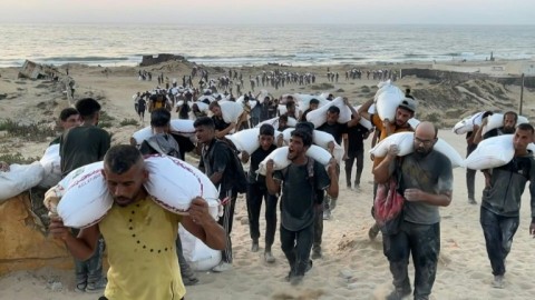 Palestinians carry bags of flour from aid convoys in the Israeli-controlled Zikim border crossing in the northern Gaza Strip