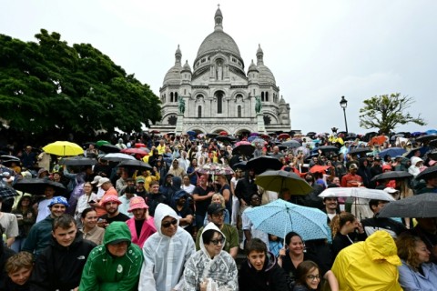 Spectators gather under umbrellas as they await the arrival of the Tour de France riders at the Sacre-Coeur basilica in Montmartre