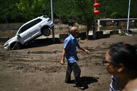 People walk past a damaged car from floods over the past few days in Huairou district, on the outskirts of Beijing on July 30, 2025
