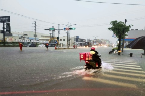 A delivery worker rides a scooter through a flooded intersection in Tainan