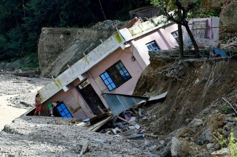 Women look at a building uprooted following heavy rains at a landslide-affected village outside Nepal's capital