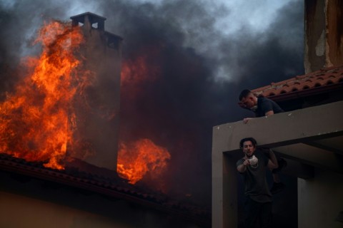 Local residents try to extinguish the fire of a burning house during a wildfire in Kryoneri near Athens