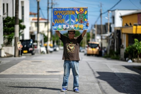 Takemasa Kinjo, who was a high school student when his mother was killed by a US Marine in 1974, holding a placard reading "Opposition to War" outside his residence in the Henoko area of Nago city