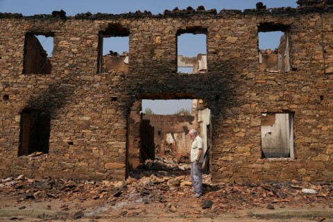 A man stands in front of a ruined burnt house after a wildfire in the village of Castrocalbon, northwestern Spain
