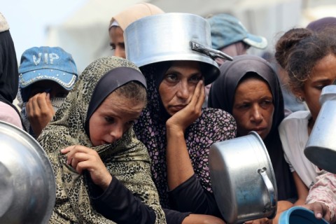 Palestinian women and children wait to receive food from a charity kitchen, in Khan Yunis in the southern Gaza Strip on August 21, 2025