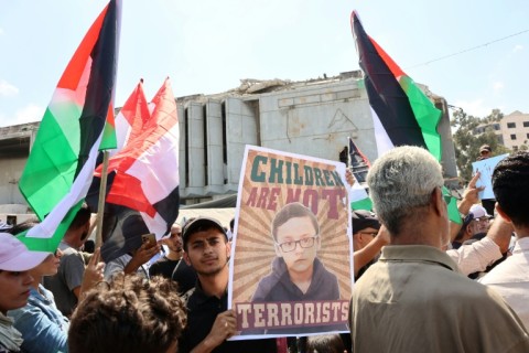 A man carries a poster as Palestinians wave their national flag in a protest in Gaza City on August 21, 2025