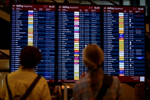 Passengers check a digital display showing flights at Berlin Brandenburg BER airport