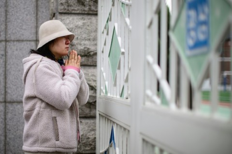 A woman weeps as she prays outside the Gwangnam High School as students sit for the annual college entrance exam