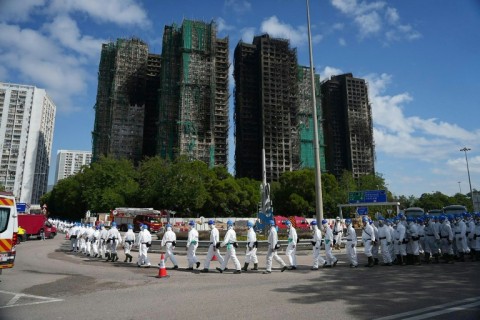 Police officers from the Disaster Victim Identification Unit (DVIU), dressed in white-coloured full-body protective gear, walk past the housing blocks of Wang Fuk Court in the aftermath of the deadly November 26 fire