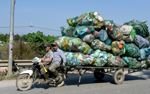 Men on a motorbike pull a cart carrying plastic waste on the outskirts of Hanoi