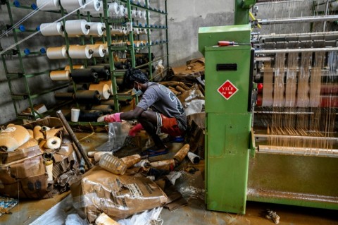 A man salvages raw materials next to a power loom at an inundated factory following flash floods in the aftermath of Cyclone Ditwah