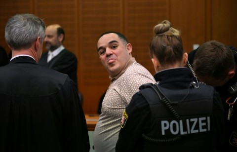 A co-defendant, Ukrainian Robert A., sticks out his tongue as he is led into the courtroom