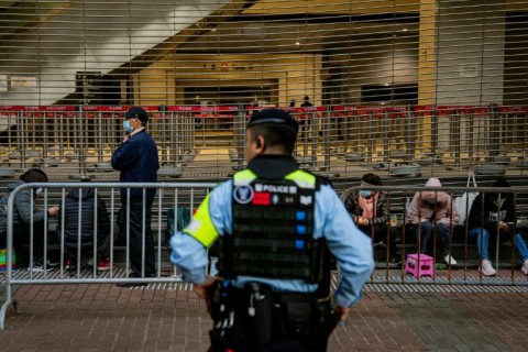 A police officer keeps watch as people wait in line to enter the West Kowloon Law Courts building