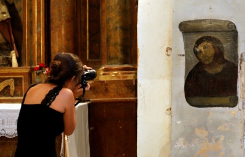 A woman takes pictures of the deteriorated version of 'Ecce Homo' after its restoration by Cecilia Gimenez
