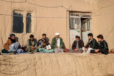 Yunus holds a picture and the son of his deceased stepbrother, Abdul Majid Haidari, while sitting with relatives outside his house in Qaisan village of Ghorian district in Herat province