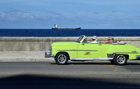 An ageing American car drives along the ocean front in Havana as an oil tanker arrives in the Cuban capital