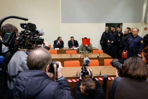 The defendant, partially identified as Farhad N., hides his face behind a folder at the start of his trial in Munich