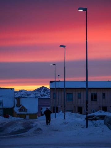 A man walks along a snow-covered street under streetlights at dusk in Nuuk, Greenland