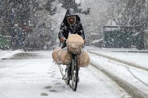 An Afghan man rides a bicycle along a road during snowfall in the green zone area of Kabul on January 22, 2026.