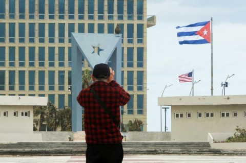 A tourist takes pictures of the US Embassy with the US flag and the Cuban flag in the background in Havana