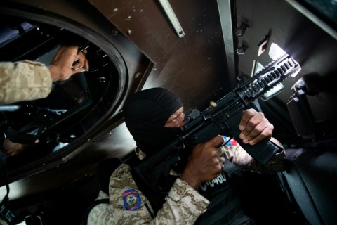 A Haitian police officer aims his weapon out a window of an armored vehicle during a patrol in downtown Port-au-Prince in January 2026