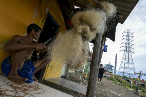 A man repairs a net to catch crabs in front of his house near the Cirebon-1 coal power plant in a fishing village in Cirebon, West Java