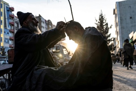 An Afghan barber trims a customer's hair along a sidewalk in Kabul