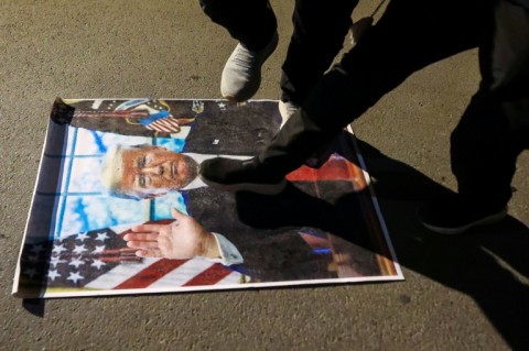 Demonstrators against the war in Iran trample on a portrait of US President Donald Trump during a protest as they march toward the US embassy in Baghdad
