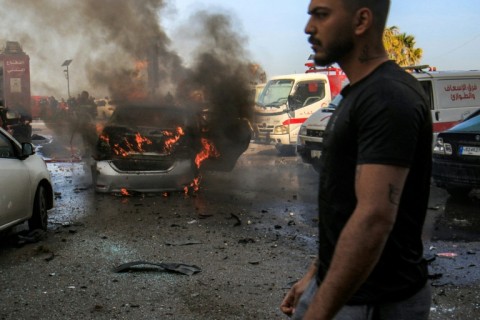 A man walks near a burning vehicle that was targeted by Israeli bombardment in Lebanon's southern coastal city of Sidon on March 18, 2026.