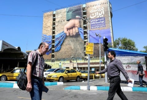 Iranians walk past a large billboard referring to the Strait of Hormuz in Tehran's Vanak Square on April 15, 2026