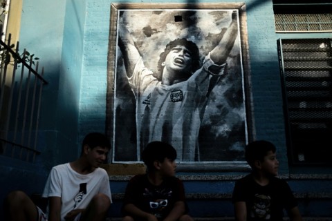 Boys sit in front of a mural depicting the late football star Diego Maradona in his childhood Buenos Aires suburb of Villa Fiorito