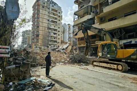 A bulldozer clears the rubble from the site of an Israeli airstrike as people return to Beirut's southern suburbs