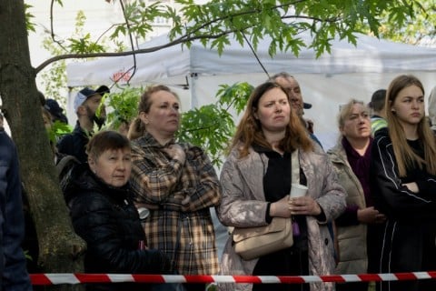 Local residents wait outside a partially destroyed residential building following the Kyiv attack