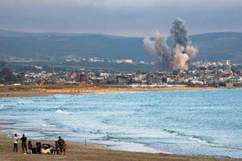 People visit beach against the backdrop of smoke rising from the site of an Israeli strike near the southern Lebanese city of Tyre on May 27